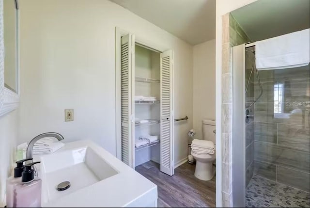 bathroom featuring hardwood / wood-style floors, toilet, sink, and a tile shower