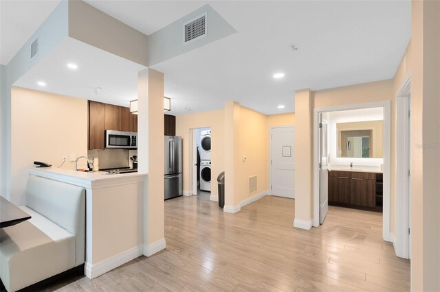 kitchen with appliances with stainless steel finishes, stacked washing maching and dryer, light hardwood / wood-style floors, and sink