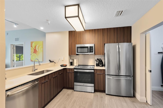 kitchen with sink, light hardwood / wood-style flooring, a textured ceiling, appliances with stainless steel finishes, and kitchen peninsula