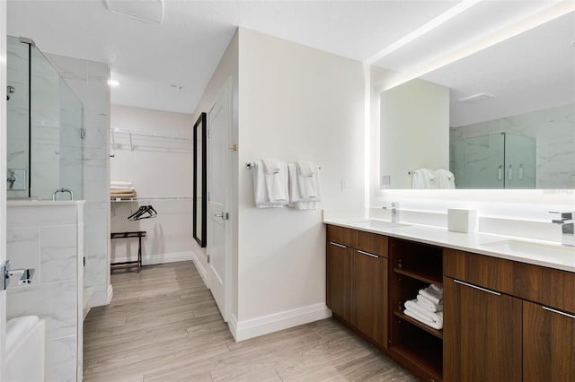 bathroom with double vanity, wood finished floors, a marble finish shower, and a sink