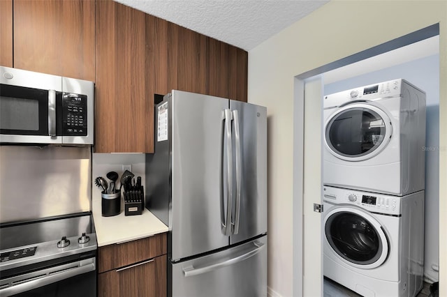 kitchen featuring modern cabinets, a textured ceiling, stacked washing maching and dryer, stainless steel appliances, and light countertops