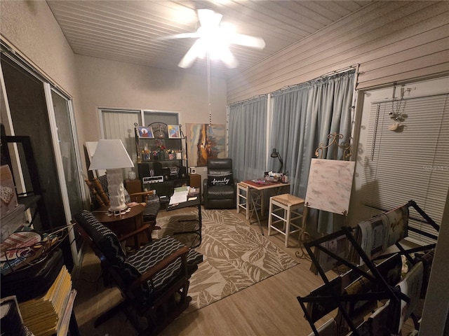 sitting room with ceiling fan, wooden walls, and wood-type flooring