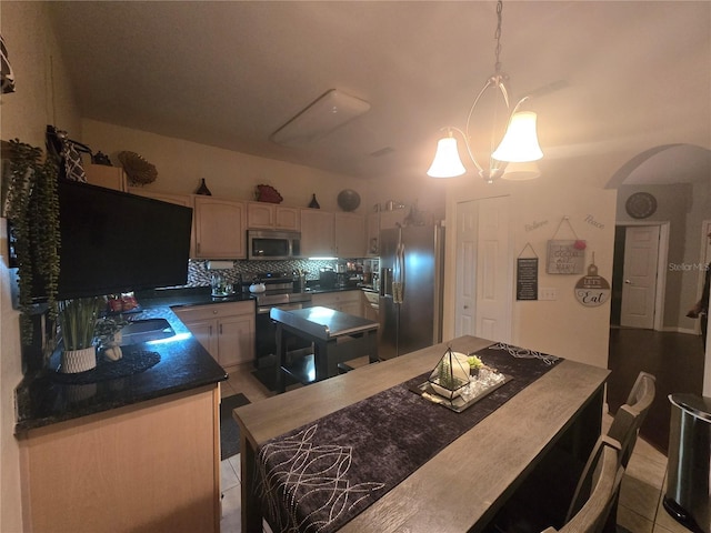 kitchen featuring appliances with stainless steel finishes, backsplash, an inviting chandelier, a center island, and hanging light fixtures