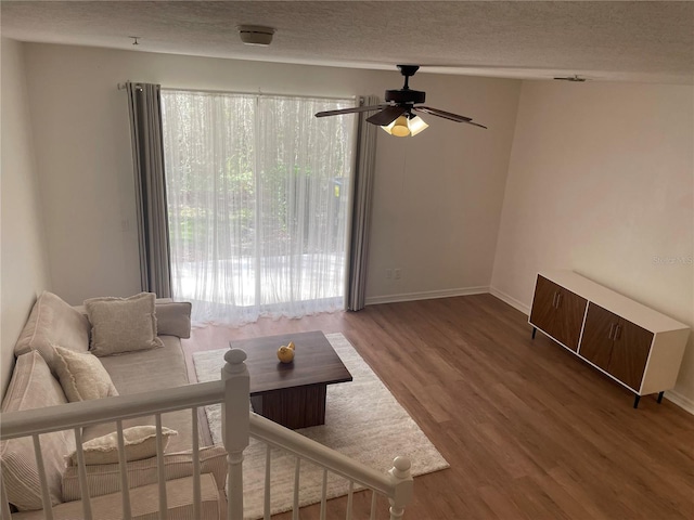 living room featuring hardwood / wood-style flooring, ceiling fan, and a textured ceiling