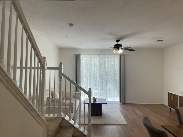 staircase with ceiling fan, hardwood / wood-style floors, and a textured ceiling