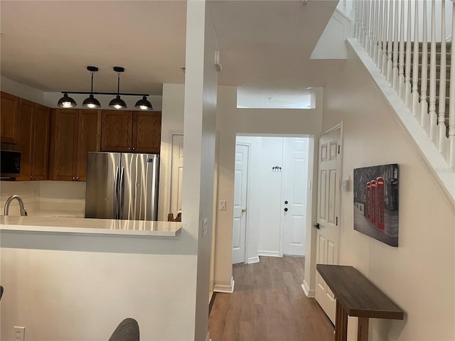 kitchen with pendant lighting, sink, hardwood / wood-style flooring, stainless steel fridge, and kitchen peninsula