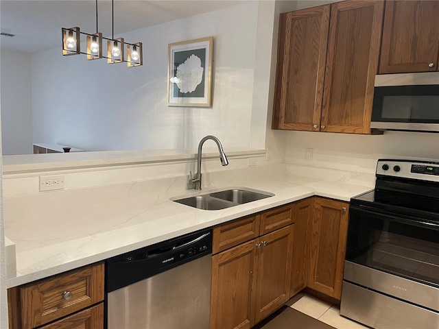 kitchen featuring light tile patterned flooring, sink, light stone counters, appliances with stainless steel finishes, and pendant lighting