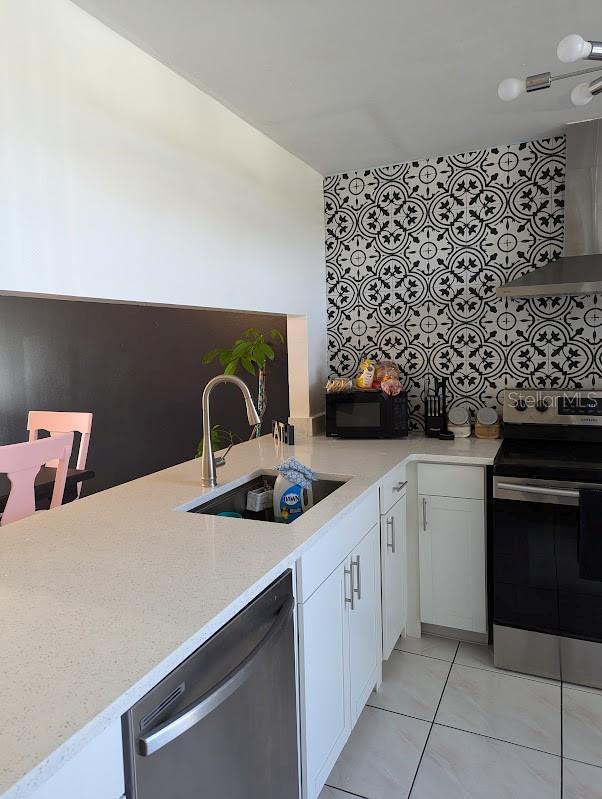 kitchen with sink, range hood, light stone counters, white cabinetry, and stainless steel appliances