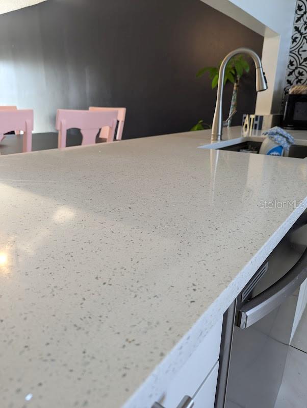 details featuring stainless steel dishwasher, white cabinets, light stone countertops, and sink