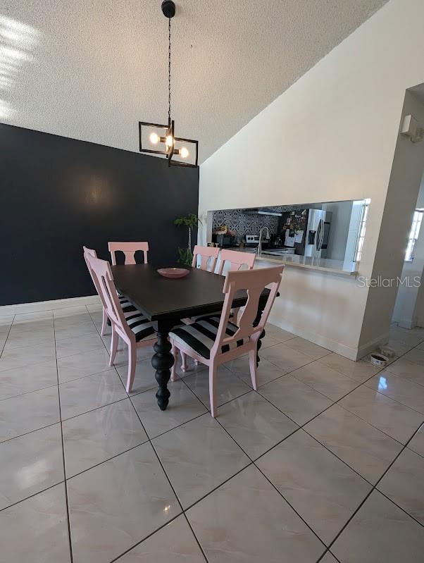 tiled dining area featuring sink, high vaulted ceiling, and a textured ceiling