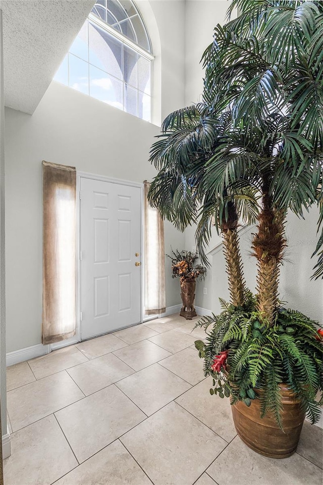 foyer entrance featuring light tile patterned flooring, a textured ceiling, a high ceiling, and baseboards