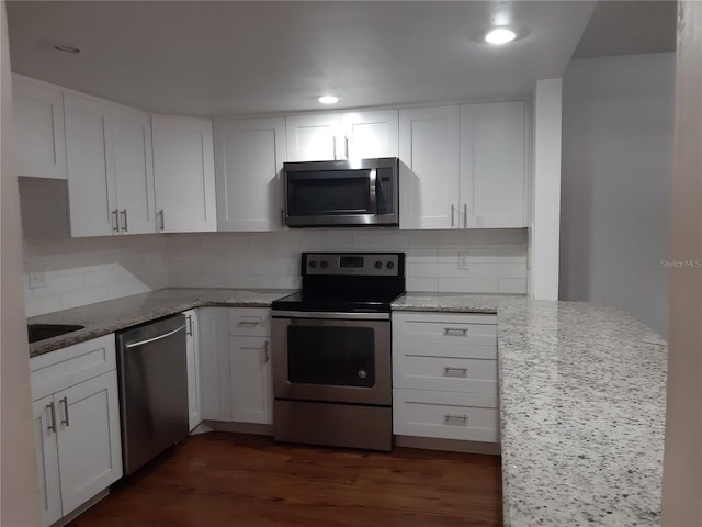 kitchen with white cabinetry, stainless steel appliances, light stone counters, dark hardwood / wood-style floors, and decorative backsplash