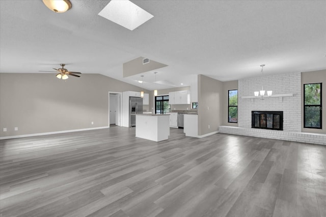 unfurnished living room with a textured ceiling, vaulted ceiling, a fireplace, ceiling fan with notable chandelier, and hardwood / wood-style flooring