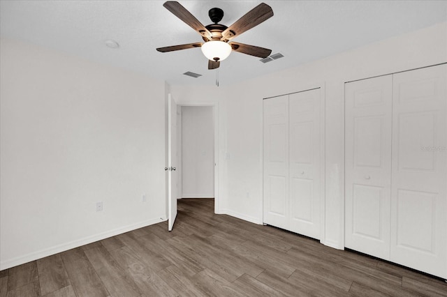 unfurnished bedroom featuring multiple closets, dark hardwood / wood-style floors, and ceiling fan