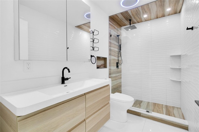 bathroom with toilet, tile patterned flooring, vanity, and tiled shower