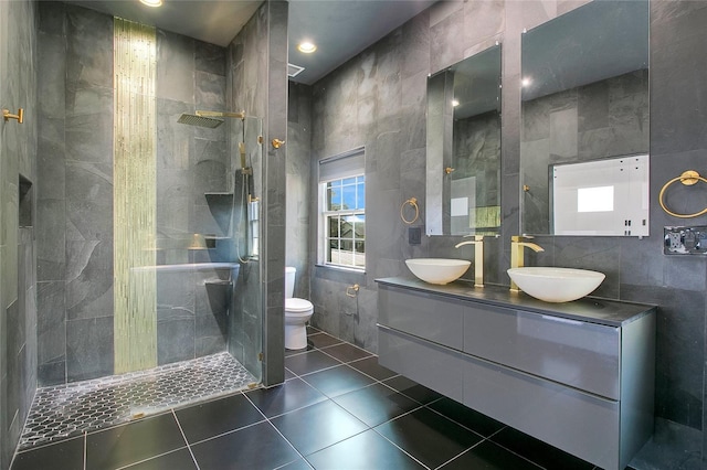 bathroom featuring vanity, tile patterned flooring, toilet, tiled shower, and tile walls