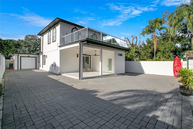 rear view of property featuring a balcony, a garage, ceiling fan, and a patio area