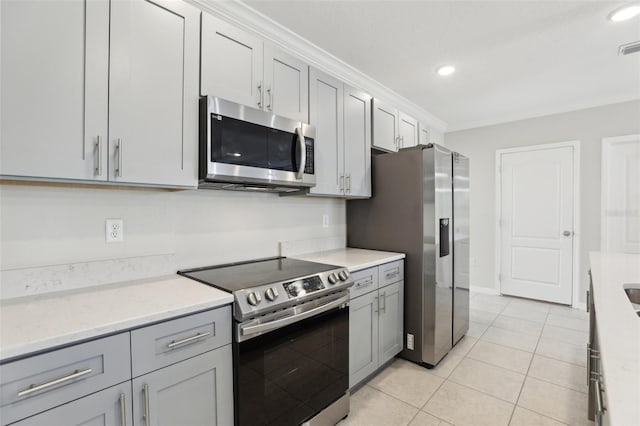 kitchen with gray cabinetry, light tile patterned floors, ornamental molding, appliances with stainless steel finishes, and light stone counters