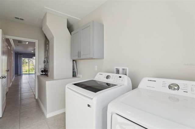 washroom featuring washing machine and clothes dryer, light tile patterned floors, and cabinets