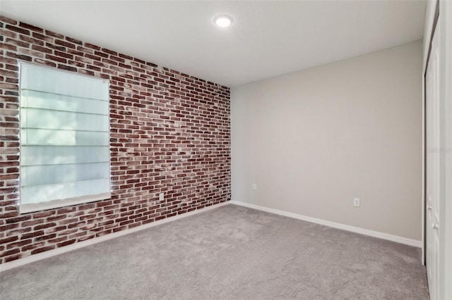 carpeted empty room featuring brick wall