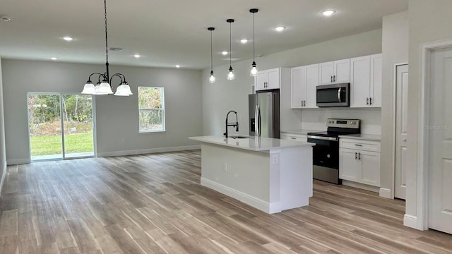 kitchen with stainless steel appliances, a kitchen island with sink, pendant lighting, a notable chandelier, and white cabinetry