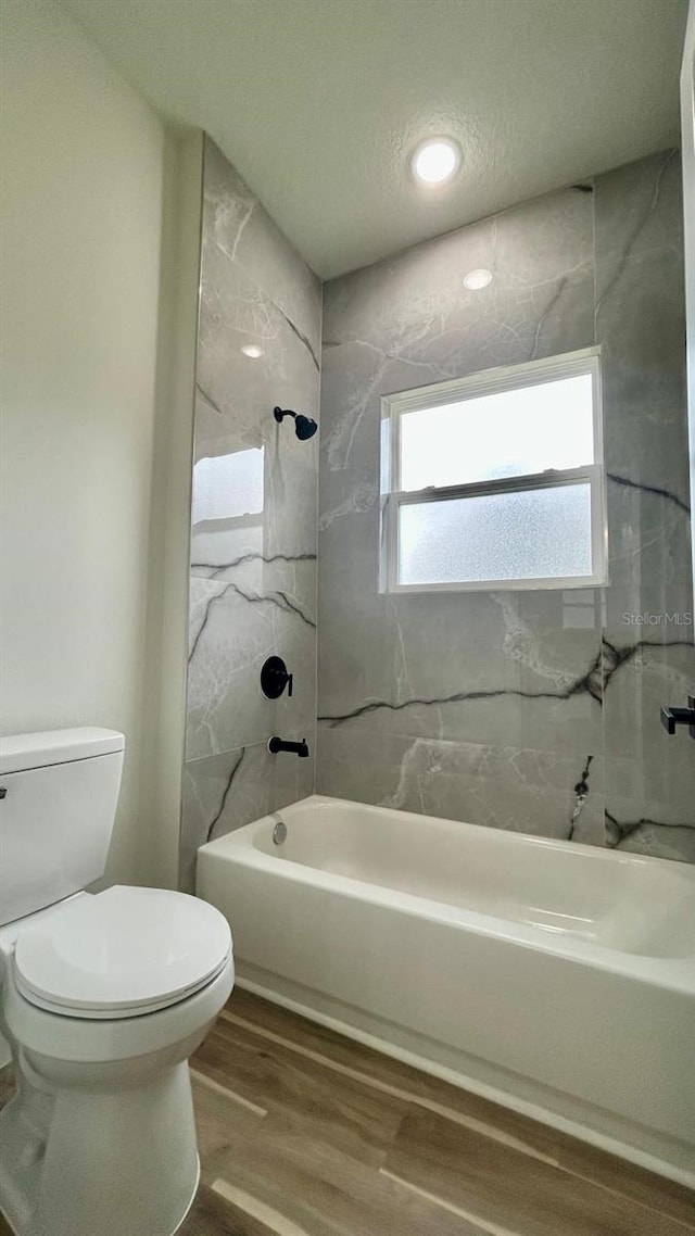 bathroom with tiled shower / bath combo, toilet, wood-type flooring, and a textured ceiling