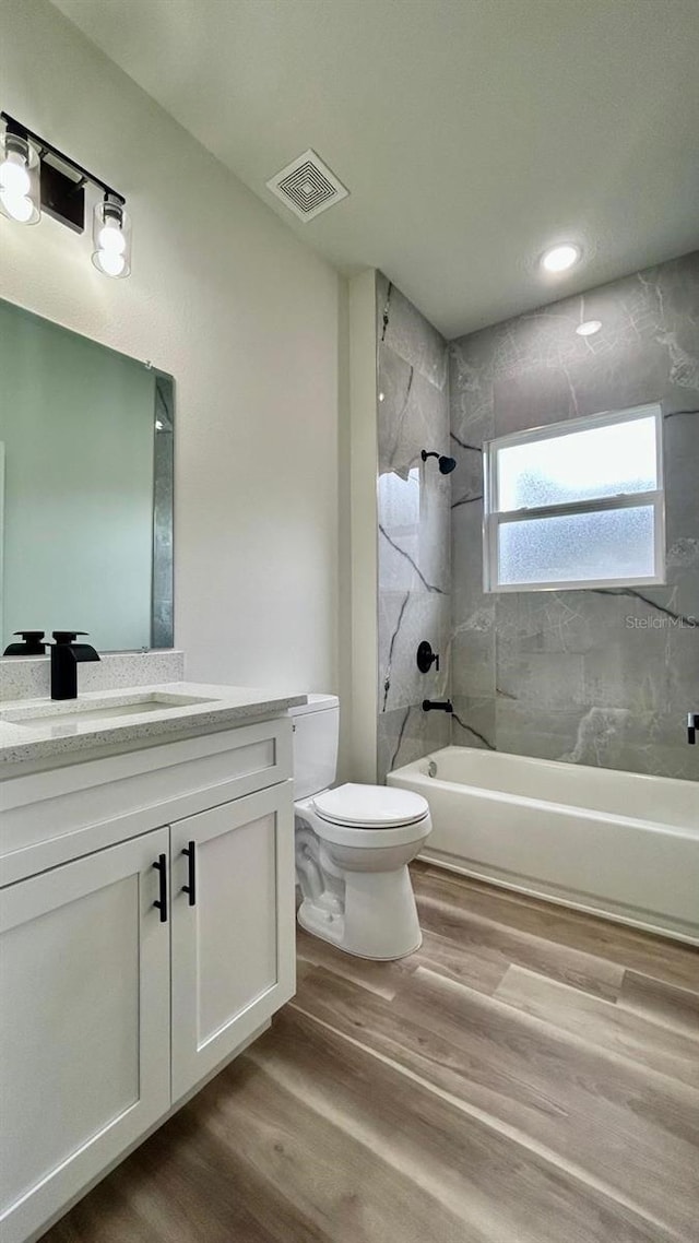 full bathroom with hardwood / wood-style flooring, tiled shower / bath combo, toilet, and vanity