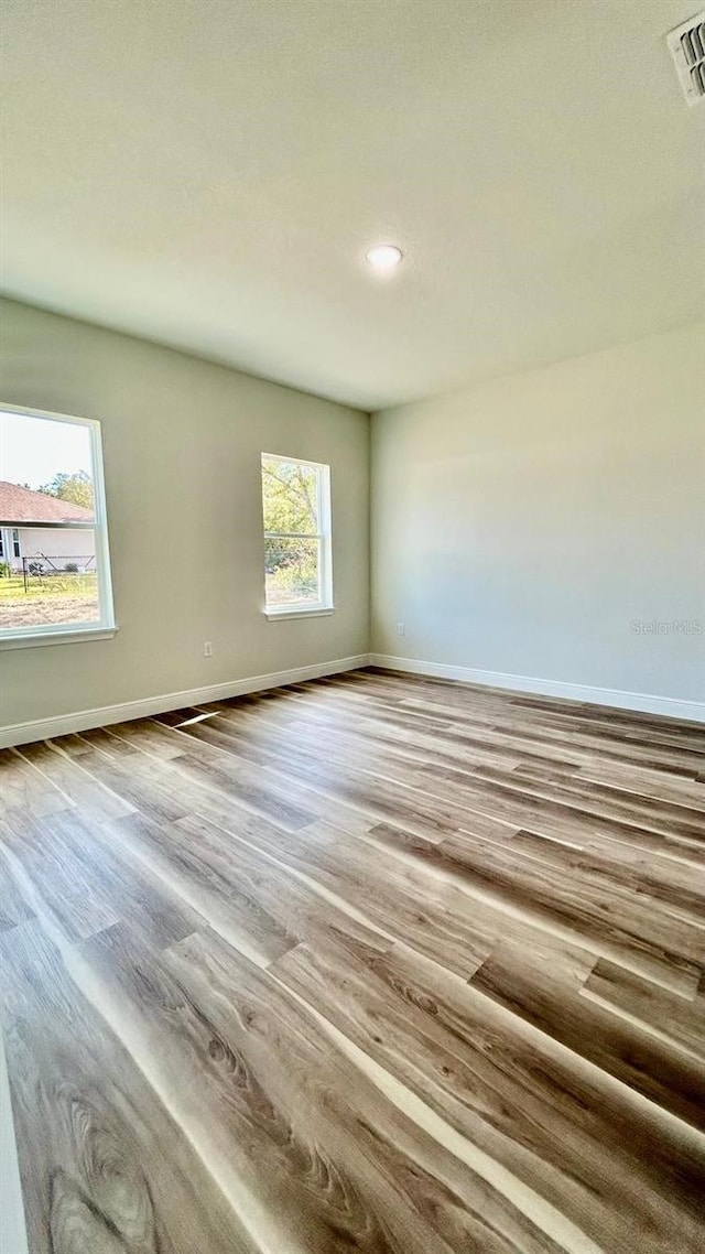 unfurnished room featuring wood finished floors, visible vents, and baseboards