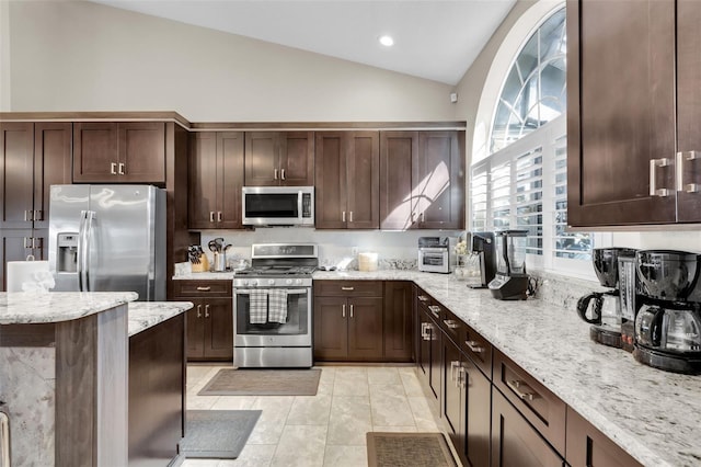 kitchen featuring lofted ceiling, dark brown cabinetry, light stone countertops, and appliances with stainless steel finishes