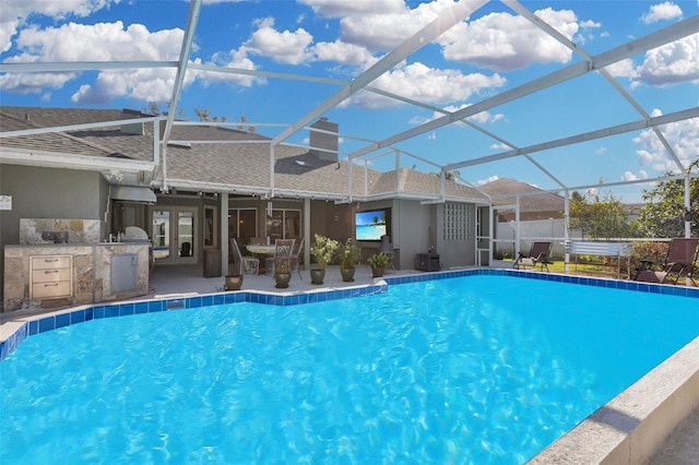 view of pool with a patio, an outdoor kitchen, and glass enclosure