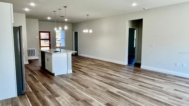 kitchen featuring white cabinetry, sink, hanging light fixtures, a notable chandelier, and an island with sink