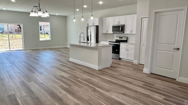 kitchen with pendant lighting, a center island with sink, white cabinets, appliances with stainless steel finishes, and a chandelier