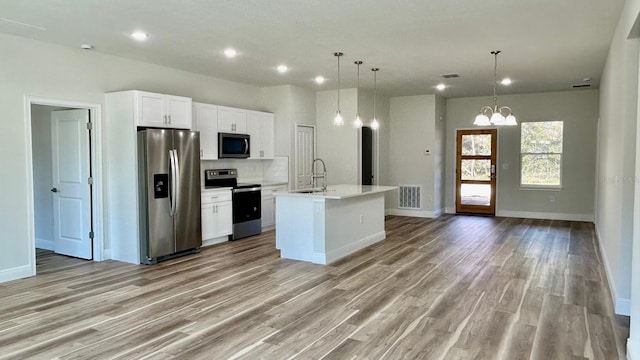 kitchen featuring a center island with sink, white cabinets, sink, appliances with stainless steel finishes, and decorative light fixtures