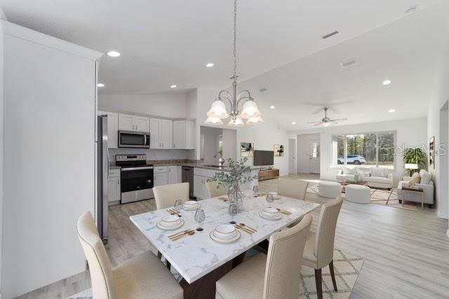 dining room featuring ceiling fan with notable chandelier, sink, light hardwood / wood-style flooring, and vaulted ceiling