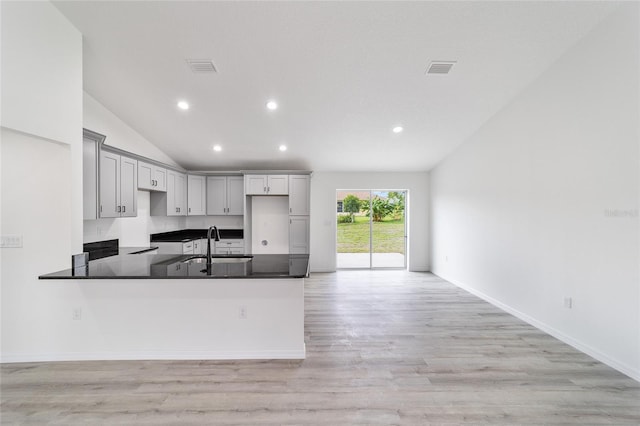 kitchen with sink, vaulted ceiling, gray cabinets, light wood-type flooring, and kitchen peninsula