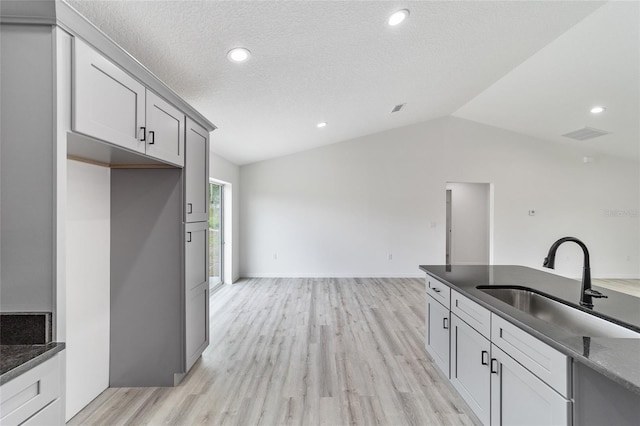 kitchen with gray cabinetry, a textured ceiling, sink, light hardwood / wood-style flooring, and lofted ceiling