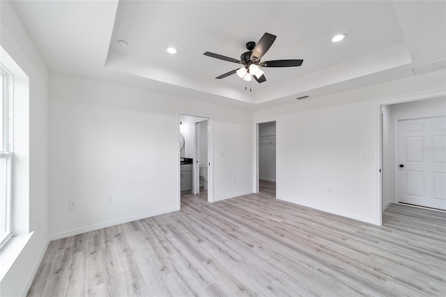 unfurnished bedroom with a raised ceiling, a walk in closet, ceiling fan, and a closet