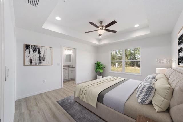 bedroom featuring ceiling fan, a raised ceiling, light wood-type flooring, and connected bathroom