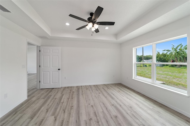 empty room with a tray ceiling, ceiling fan, and light wood-type flooring