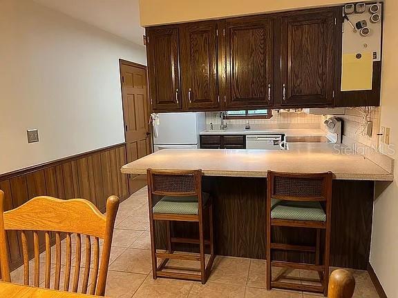 kitchen with kitchen peninsula, light tile patterned floors, white refrigerator, dishwasher, and wood walls