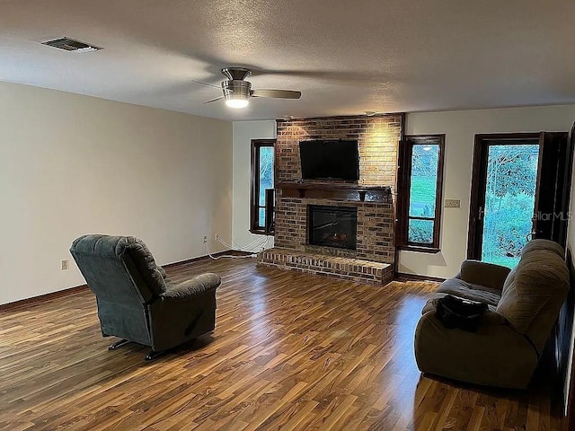 living room featuring ceiling fan, wood-type flooring, a textured ceiling, and a brick fireplace