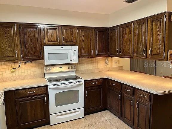 kitchen featuring backsplash, dark brown cabinets, light tile patterned flooring, and white appliances