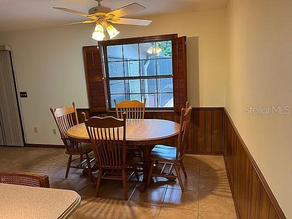 tiled dining space featuring wood walls and ceiling fan