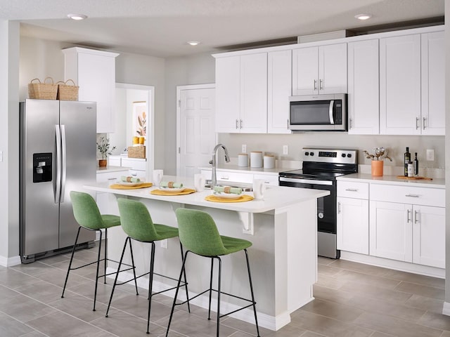 kitchen featuring appliances with stainless steel finishes, white cabinetry, a breakfast bar area, and an island with sink