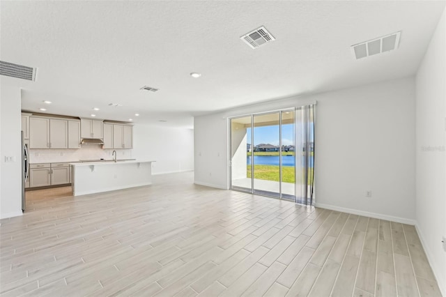 unfurnished living room featuring light hardwood / wood-style floors, a water view, and a textured ceiling