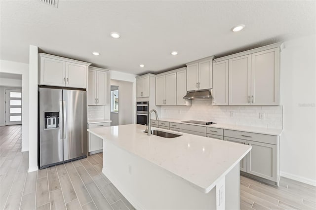 kitchen featuring a center island with sink, appliances with stainless steel finishes, light stone countertops, sink, and backsplash