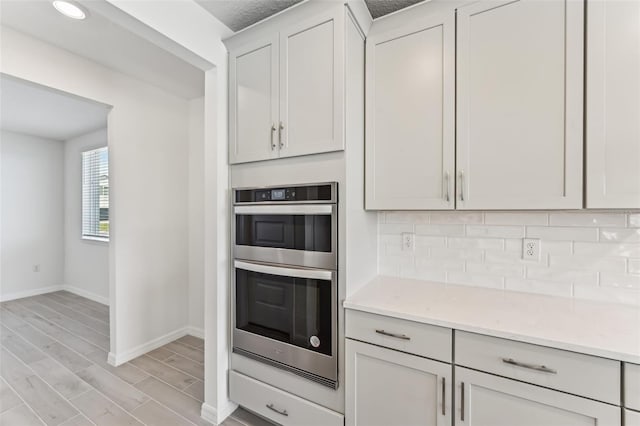 kitchen with light stone countertops, white cabinetry, stainless steel double oven, and decorative backsplash