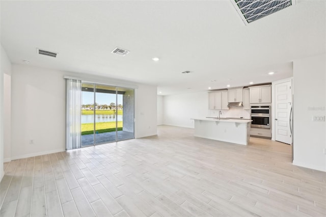 unfurnished living room featuring visible vents, light wood-style floors, and a sink