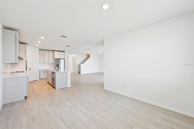 kitchen featuring visible vents, an island with sink, open floor plan, stainless steel appliances, and light countertops