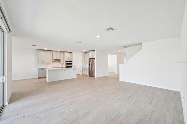 unfurnished living room featuring stairway, visible vents, recessed lighting, a sink, and light wood-style floors